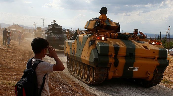 A boy salutes as Turkish Armed Forces vehicles drive pass by a village on the Turkish-Syrian border line in Reyhanli, Hatay province, Turkey October 11, 2017 © Osman Orsal / Reuters